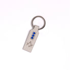 A silver-coloured keyring with a Masonic square and compasses design, embellished with blue style crystals.
