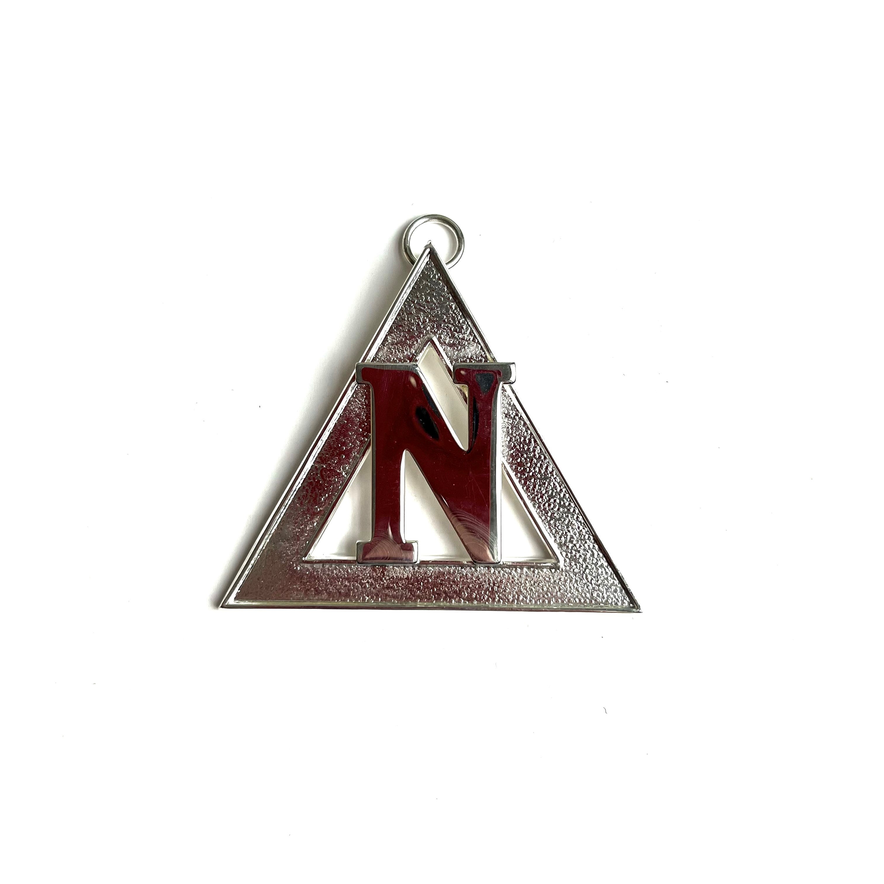 A Masonic silver-colored triangular metal collar jewel with the letter 'N' in the centre