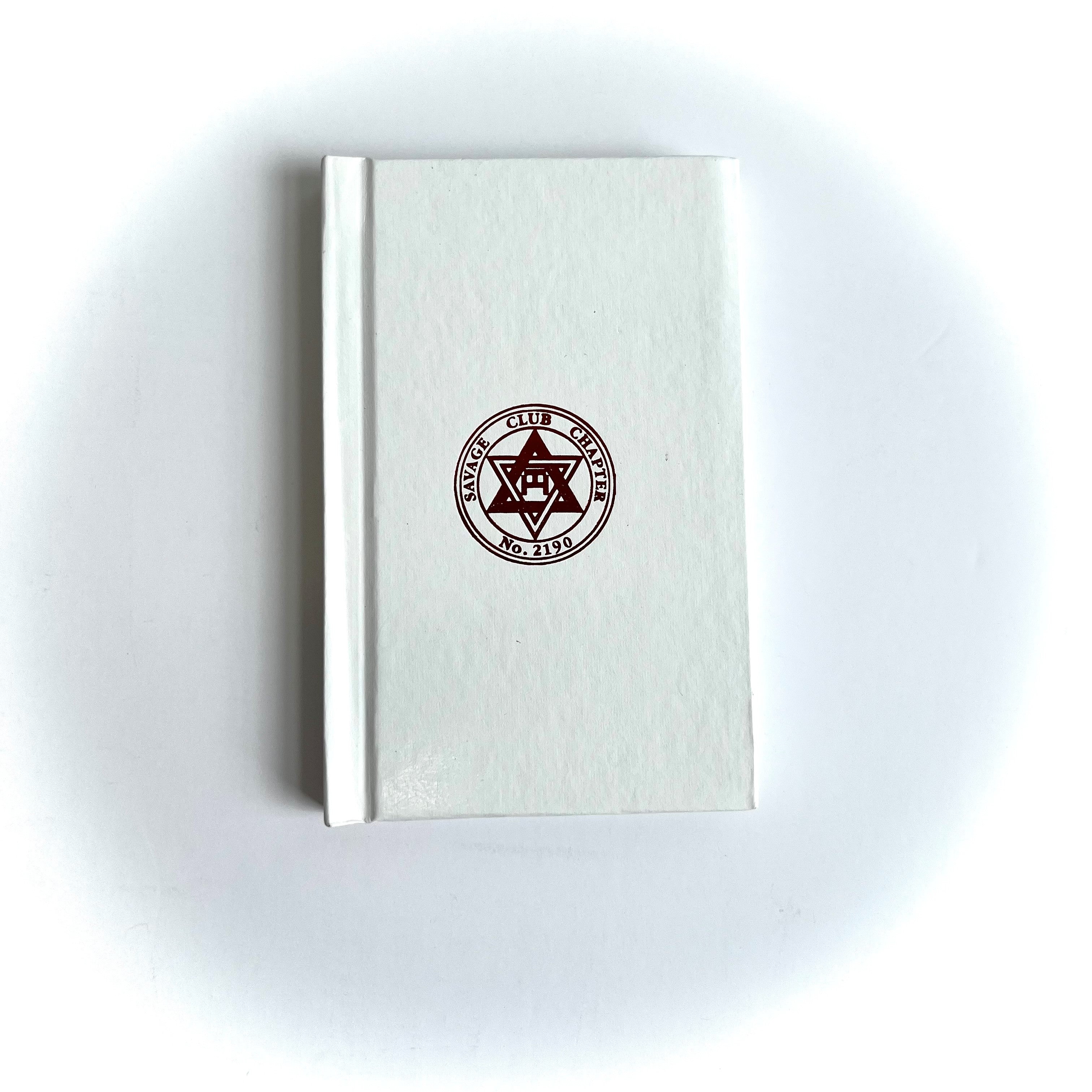 A Masonic Savage Club Royal Arch Ritual closed book with a plain beige cover, featuring a centered emblem or seal on the front.