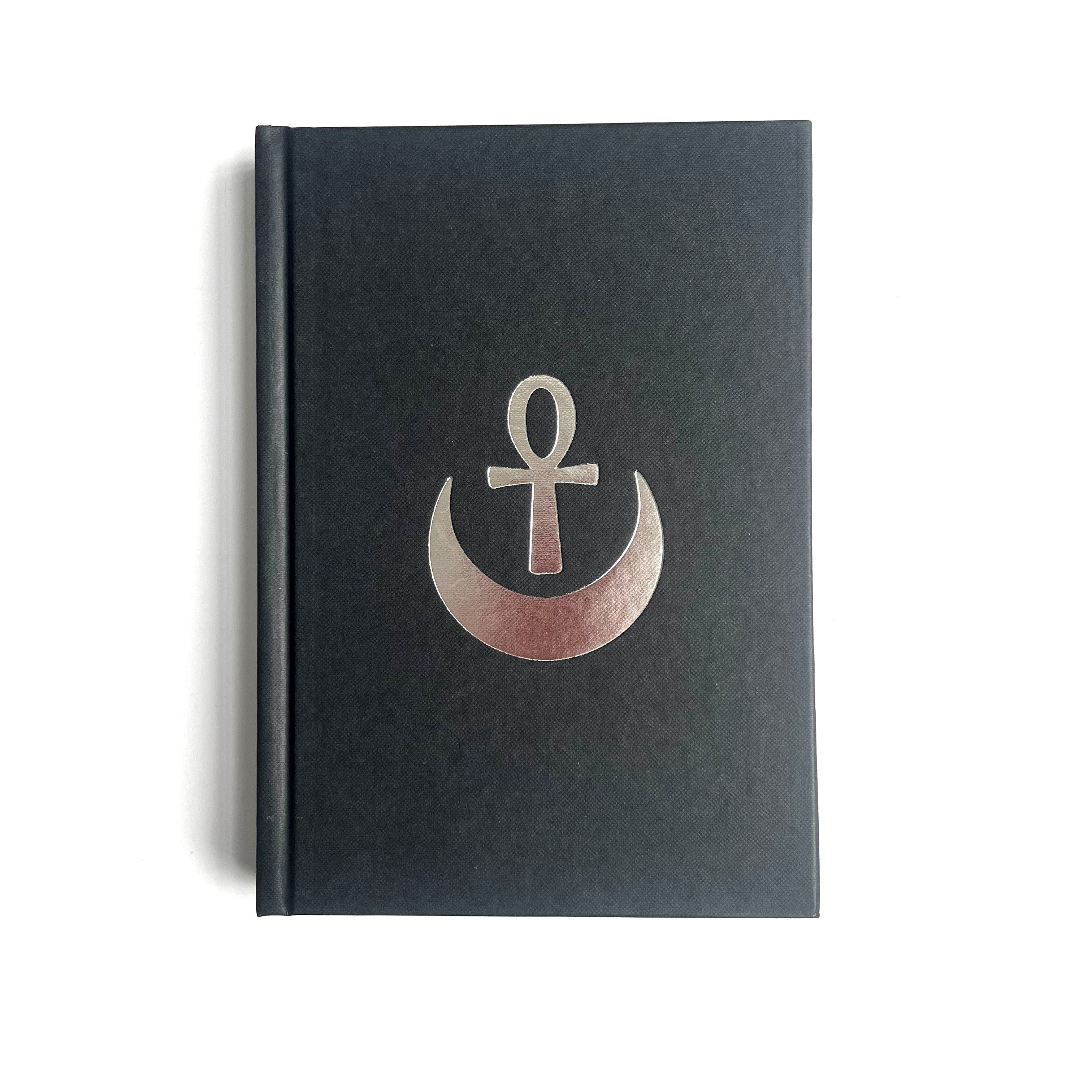 A hardback Masonic book with a black cover featuring a silver emblem of an ankh in a crescent moon.