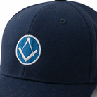 Close up view of navy blue baseball cap with a curved brim, featuring an embroidered Masonic square-and-compass symbol in white and light blue on the front.