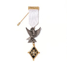 A Knight of the Holy Sepulchre Companion Breast Jewel with a white ribbon, featuring metalwork including an eagle and a shield, with a black and gold emblem at the center and a stickpin on the back.