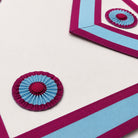 UGLE official Mark Mason Apron Close-up of pleated rosette on white Masonic apron with magenta and blue ribbon trim.