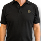 Model wearing black polo shirt with a collar and button placket, featuring a small gold embroidered Masonic square-and-compass symbol on the chest.