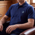 Model wearing blue polo shirt with a collar and button placket, featuring a small sliver and blue embroidered Masonic square-and-compass symbol on the chest.