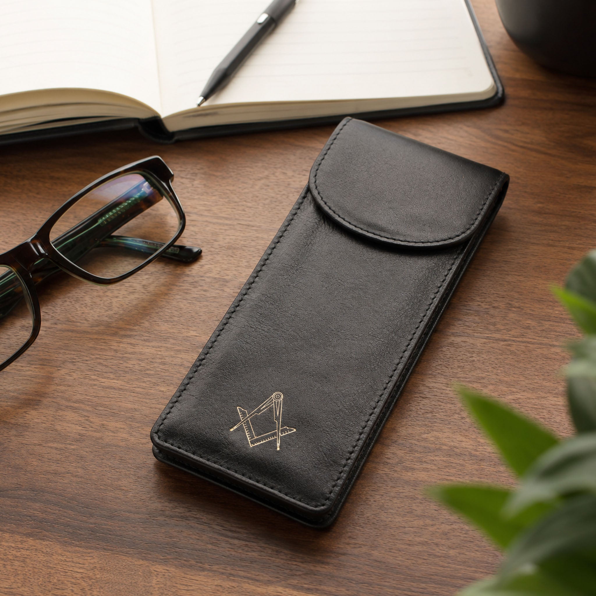 Black leather masonic glasses case on wooden desk with reading glasses and notebook