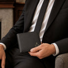 Man in a black suit holding a black Masonic wallet with a gold Square and Compasses emblem.