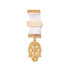 A gold-colored Masonic breast jewel with a white ribbon attachment and intricate detailing.