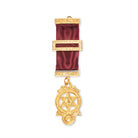 A gold-colored Masonic breast jewel with a geometric pattern and a red ribbon attachment, displaying a symbolical design.