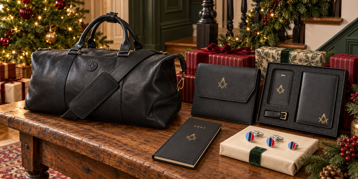 Masonic Christmas gifts displayed beside a decorated tree, including a black leather holdall, travel set, jewel holder, 2027 diary, One Journey cufflinks and lapel pin.